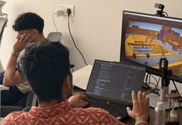 A developer working through a build on a laptop, with a game scene up on the monitor behind, at the Hands-on Developer Edition session.